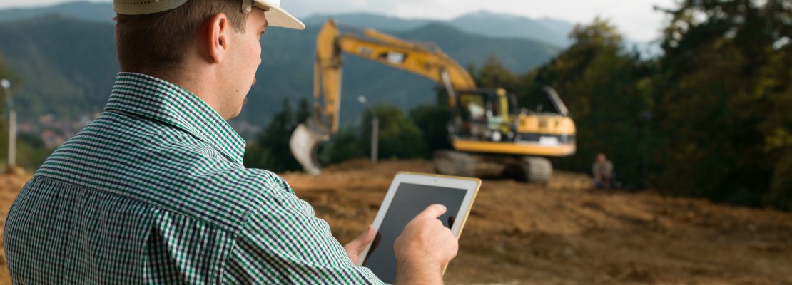 back view of caucasian engineer standing on construction site checking plan on digital tablet